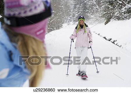 Smiling young woman on ski-slope wearing snow-shoes, with friend watching in foreground View Large Photo Image Stock Image - Smiling young woman on ski-slope wearing snow-shoes, with friend watching in foreground. Fotosearch