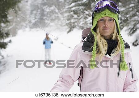 Smiling young woman on ski-slope, person in background, portrait View Large Photo Image Stock Photograph - Smiling young woman on ski-slope, person in background, portrait. Fotosearch