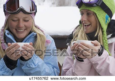 Stock Image - Two young blonde women in ski-wear holding cups of hot chocolate. Fotosearch
