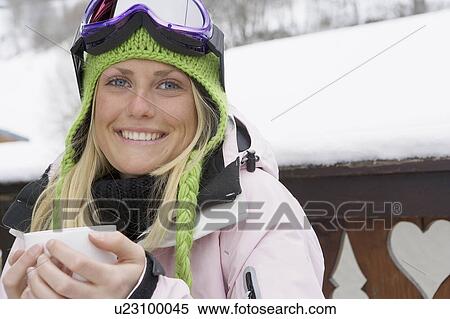 Stock Photography - Young woman in ski-wear, holding cup. Close-up, high angle, portrait. Fotosearch