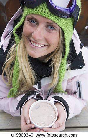 Stock Image - Young woman in ski-wear with cup of hot chocolate, close-up, high angle, portrait. Fotosearch