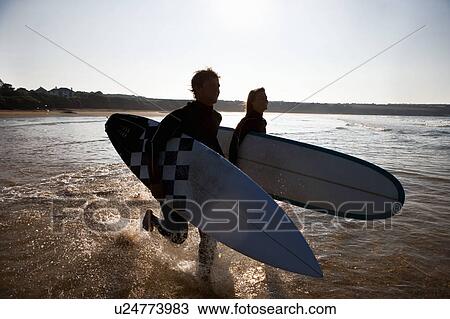 Couple running through the water with surfboards smiling. View Large Photo Image Stock Image - Couple running through the water with surfboards smiling.. Fotosearch