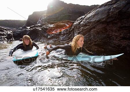 Stock Photography - Four people lying on surfboards in the water smiling.. Fotosearch