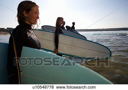 Four people standing with surfboards in the water smiling. View Large Photo Image Stock Photo - Four people standing with surfboards in the water smiling.. Fotosearch