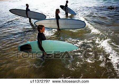 Stock Photo - Four people standing with surfboards in the water smiling.. Fotosearch