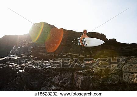 Man holding surfboard on large rocks. View Large Photo Image Stock Image - Man holding surfboard on large rocks.. Fotosearch