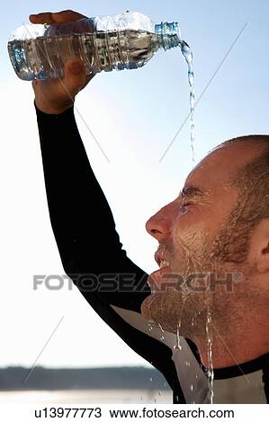 Stock Image - Man in wetsuit pouring water on his face.. Fotosearch