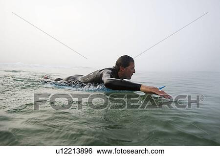 Man lying on surfboard in the water. View Large Photo Image Stock Photograph - Man lying on surfboard in the water.. Fotosearch