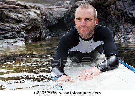 Stock Photograph - Man lying on surfboard in the water.. Fotosearch