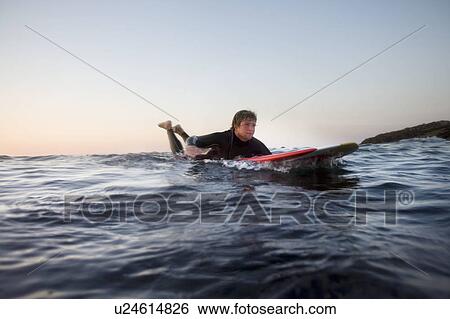 Stock Photograph - Man lying on surfboard in the water.. Fotosearch