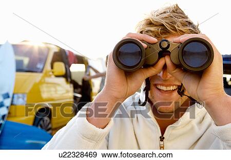 Stock Photo - Man on beach with binoculars smiling with woman unloading van at the beach.. Fotosearch