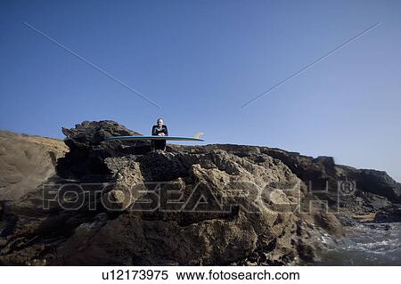 Man sitting with surfboard on large rocks smiling. View Large Photo Image Stock Photography - Man sitting with surfboard on large rocks smiling.. Fotosearch
