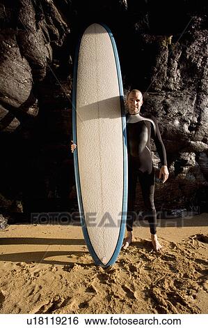 Stock Photograph - Man standing with surfboard smiling.. Fotosearch