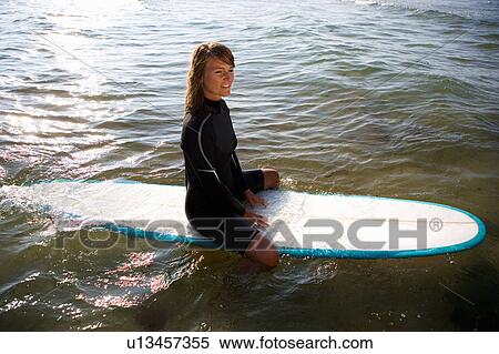 Stock Photography - Woman sitting on a surfboard smiling.. Fotosearch