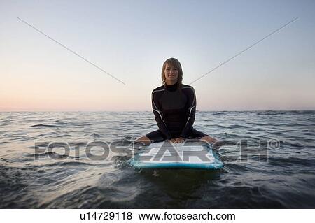 Stock Photo - Woman sitting on surfboard in the water smiling.. Fotosearch