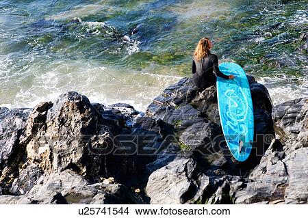Woman sitting with a surfboard on large rocks. View Large Photo Image Picture - Woman sitting with a surfboard on large rocks.. Fotosearch