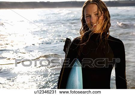 Woman standing with a surfboard smiling. View Large Photo Image Stock Image - Woman standing with a surfboard smiling.. Fotosearch