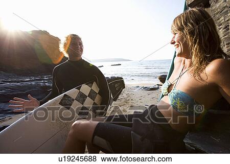 Stock Photo - Couple laughing at the beach with man holding a surfboard.. Fotosearch