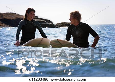 Couple sitting on surfboards in the water smiling. View Large Photo Image Stock Photograph - Couple sitting on surfboards in the water smiling.. Fotosearch