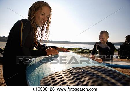 Stock Photograph - Couple waxing their surfboards smiling.. Fotosearch