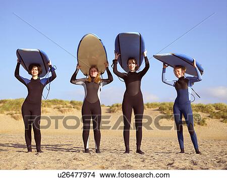 Picture - Four female surfers standing on a beach.. Fotosearch