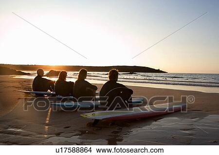 Picture - Four people sitting on the beach with surfboards.. Fotosearch