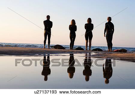 Four people standing on the beach with surfboards. View Large Photo Image Stock Image - Four people standing on the beach with surfboards.. Fotosearch