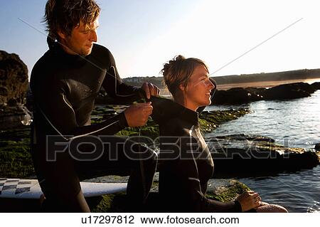 Man helping woman with wetsuit by the water. View Large Photo Image Stock Image - Man helping woman with wetsuit by the water.. Fotosearch