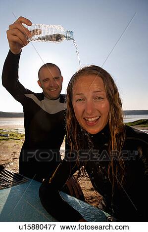 Stock Photo - Man pouring water over laughing woman's head with her surfboard on lap.. Fotosearch