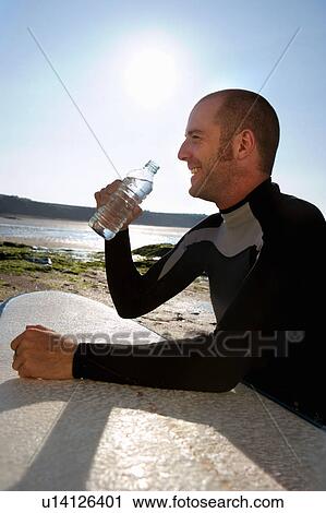 Man sitting with surfboard drinking water smiling. View Large Photo Image Stock Image - Man sitting with surfboard drinking water smiling.. Fotosearch