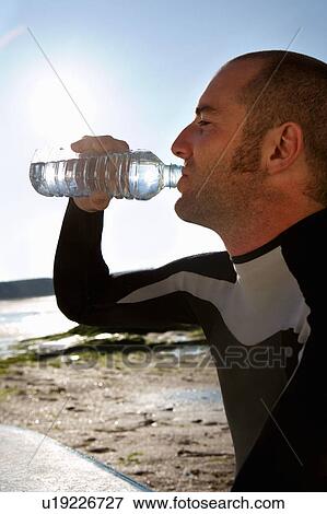 Man sitting with surfboard drinking water. View Large Photo Image Stock Photo - Man sitting with surfboard drinking water.. Fotosearch