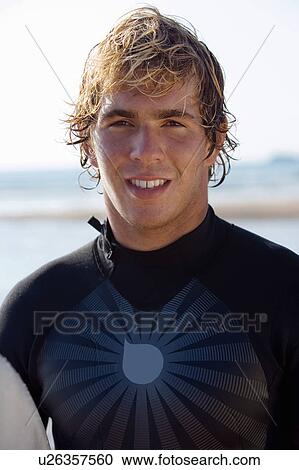 Stock Image - Man standing with surfboard on beach.. Fotosearch