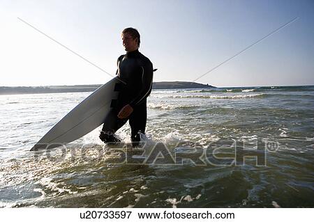 Man walking with a surfboard in the water smiling. View Large Photo Image Stock Photo - Man walking with a surfboard in the water smiling.. Fotosearch