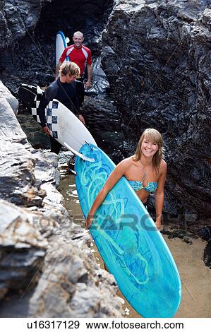 Three people carrying surfboards by large rocks smiling. View Large Photo Image Stock Photo - Three people carrying surfboards by large rocks smiling.. Fotosearch
