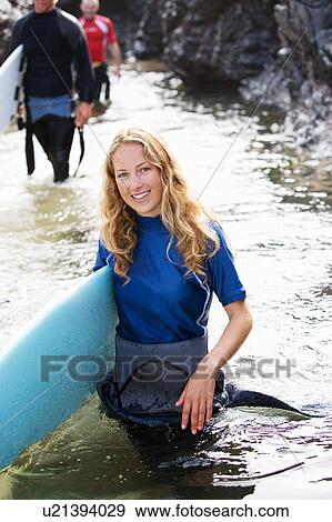 Stock Photo - Three people carrying surfboards through water smiling.. Fotosearch