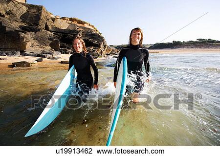 Two women carrying surfboards in the water smiling. View Large Photo Image Stock Image - Two women carrying surfboards in the water smiling.. Fotosearch