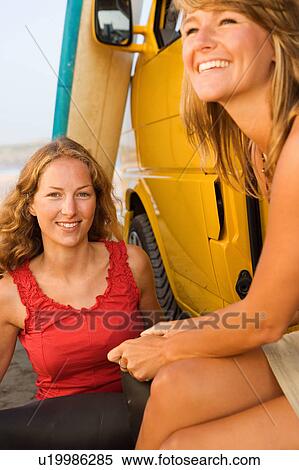 Two women sitting by a van smiling with surfboards in background. View Large Photo Image Stock Photography - Two women sitting by a van smiling with surfboards in background.. Fotosearch
