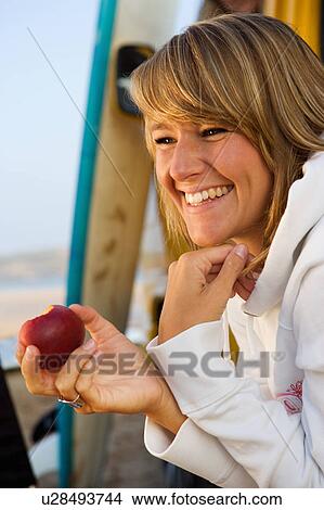 Picture - Woman eating an apple near surfboards.. Fotosearch