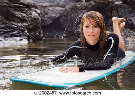 Stock Photo - Woman lying on surfboard in the water.. Fotosearch