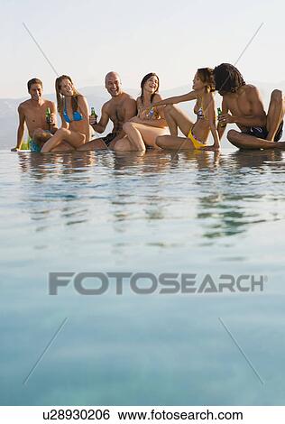 Stock Photograph - Men and women on the edge of a pool. Fotosearch