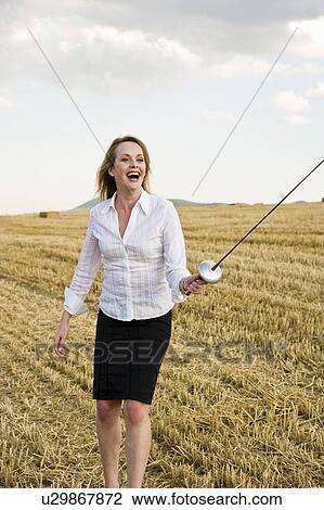 Stock Image - Businesswoman fencing in a wheat field.. Fotosearch