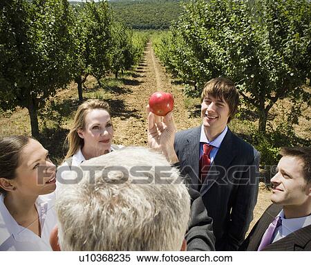 Stock Photography - Man showing apple to group in orchard.. Fotosearch