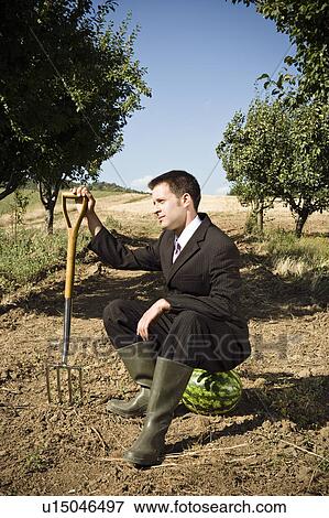 Man sitting on watermelon holding garden fork. View Large Photo Image Stock Photo - Man sitting on watermelon holding garden fork.. Fotosearch