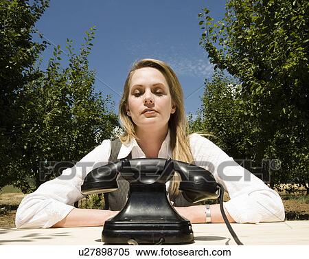 Stock Photography - Woman sitting at desk with old telephone in orchard.. Fotosearch