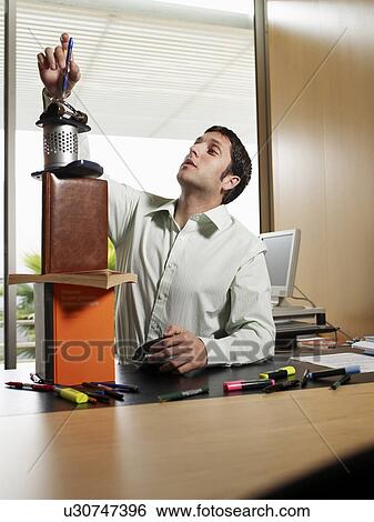 Stock Photograph - Businessman making tower of stationary equipment on desk. Fotosearch