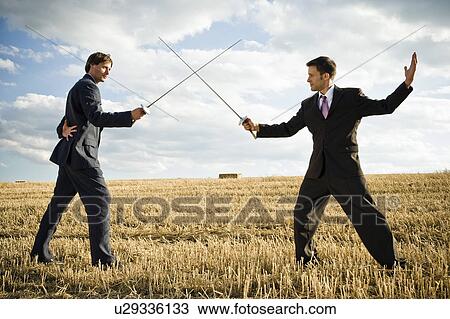 Stock Image - Businessmen fencing in wheat field.. Fotosearch