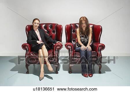 Stock Image - Businesswoman and disheveled woman in comfy leather chairs. Fotosearch