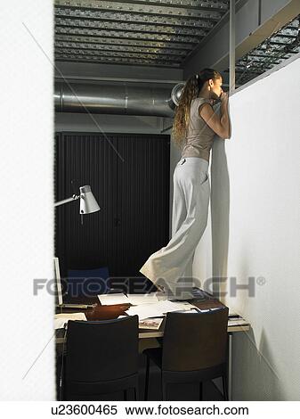 Stock Photography - Businesswoman on her desk looking into the next office. Fotosearch
