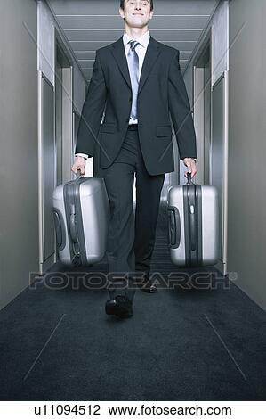 Stock Image - Man carrying suitcases in a hallway. Fotosearch