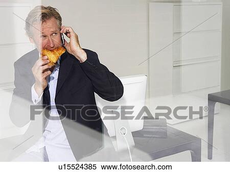 Stock Photography - Man in office eating croissant on telephone with reflections.. Fotosearch